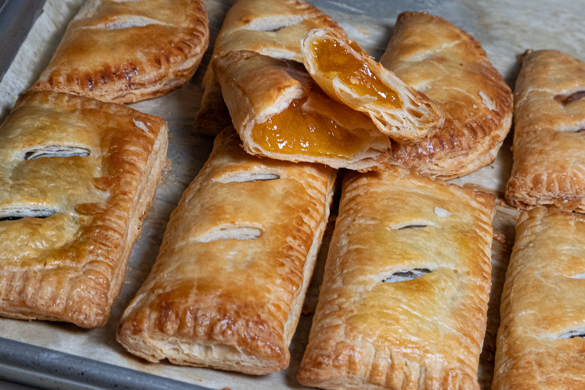 This photo shows the turnovers on a baking sheet with one opened to see the apricot filling.