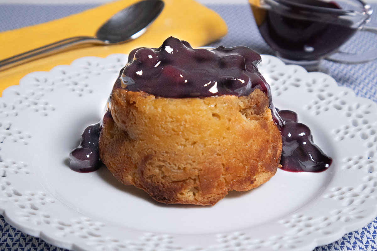 A whole single bread pudding with blueberry  sauce on a white plate with a yellow napkin and spoon,  