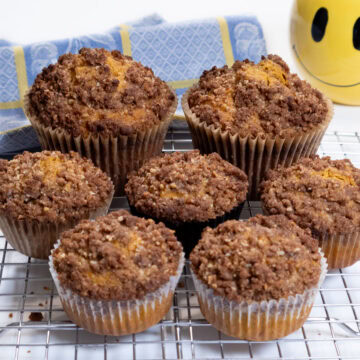 Pumpkin Muffins on a cooling rack with a blue and yellow cloth and yellow smiley face tea cup,,