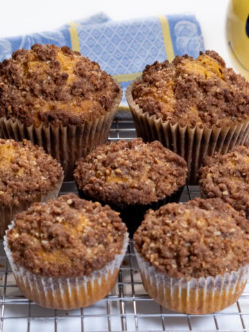 Pumpkin Muffins on a cooling rack with a blue and yellow cloth and yellow smiley face tea cup,,