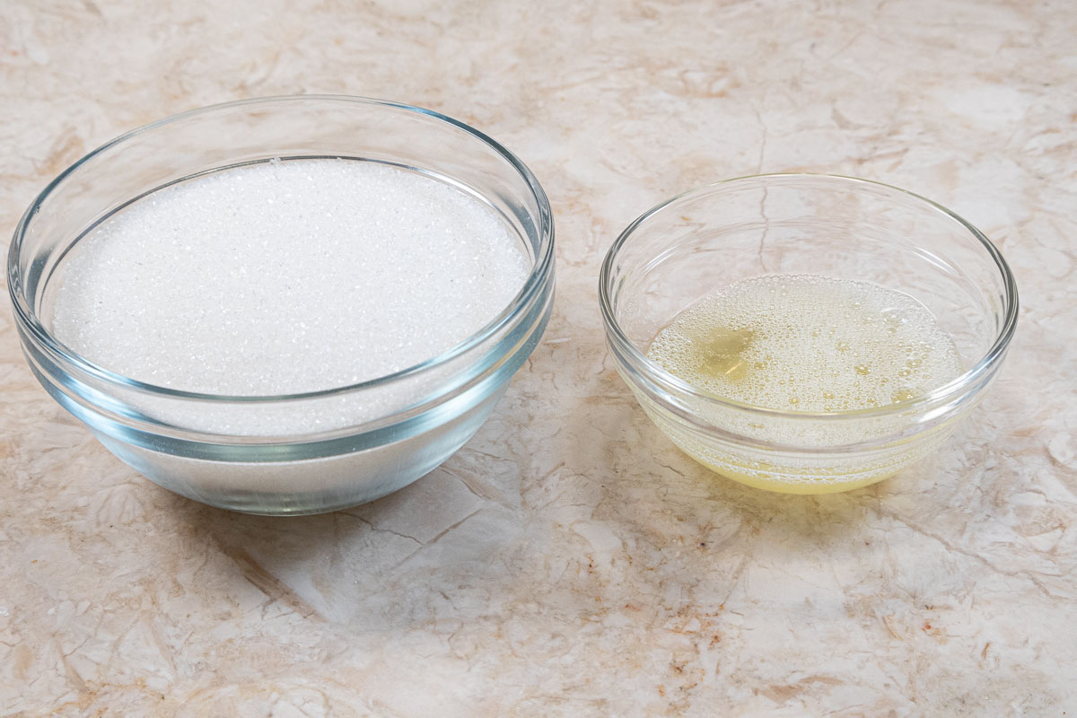 A bowl of sanding sugar and a smaller bowl of egg white on a marble table.