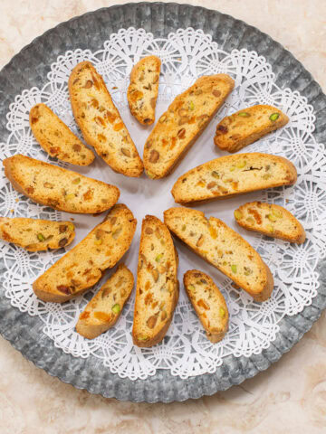 A round doilie covered tray holds large and mini Apricot Pistachio Biscotti.