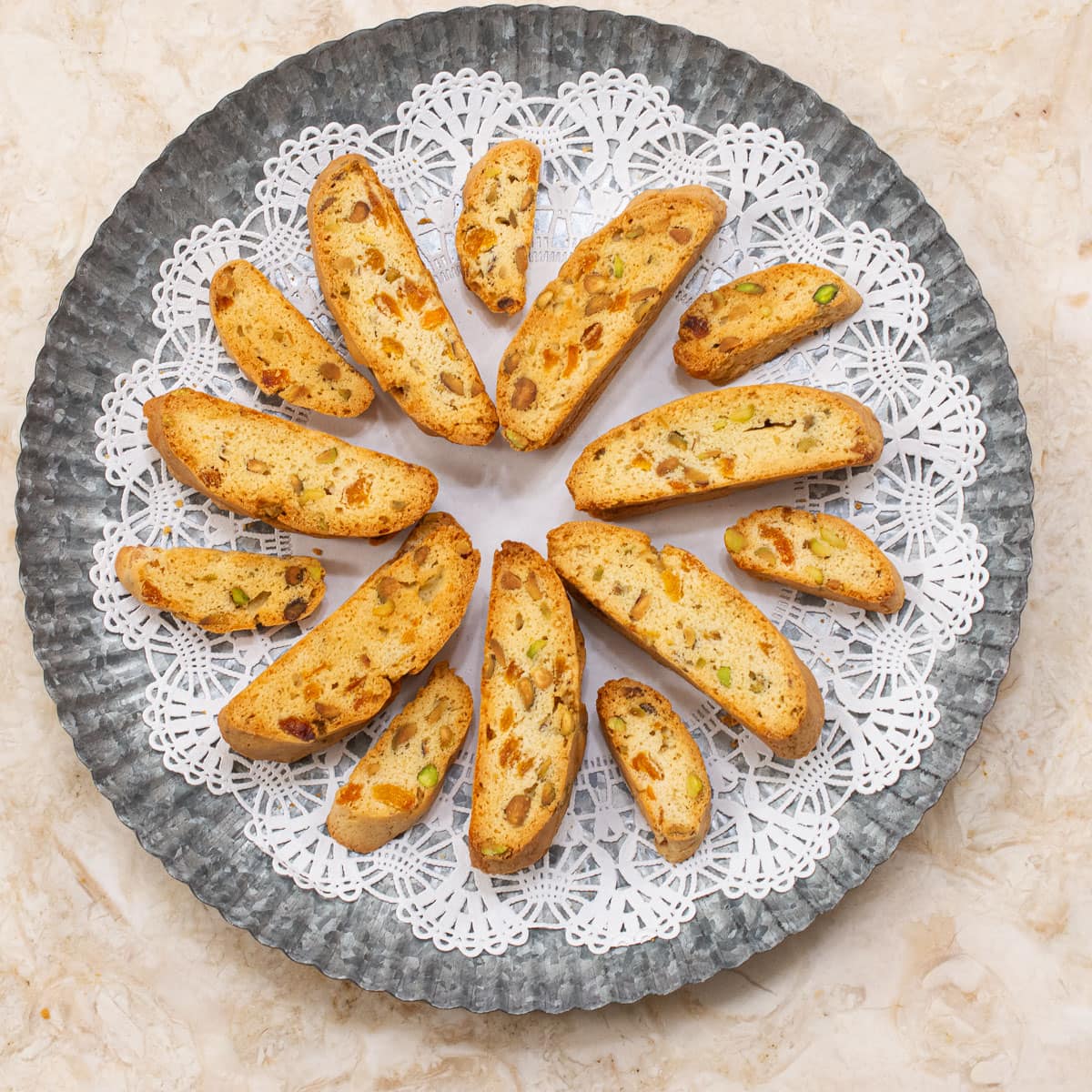 A round doilie covered tray holds large and mini Apricot Pistachio Biscotti.