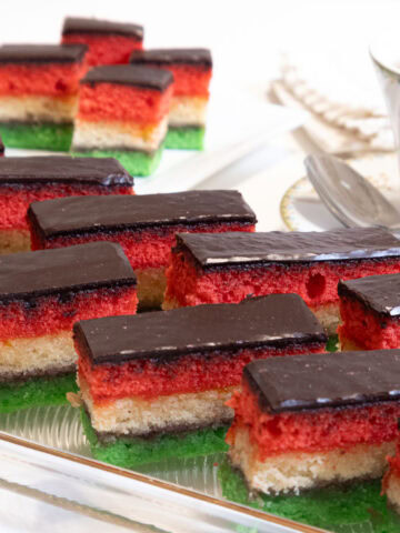 The featured picture shows a two rows on the diagonal of the Neapolitan cookies cut in bars some in the background cut in half and a cup of tea on the side.