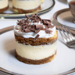 An Individual Italian Tiramisu sits on a cream colored plate and dark beige and silver trim with a cup of tea and a plater of tiramisu in the background,