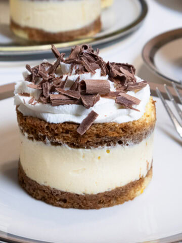 An Individual Italian Tiramisu sits on a cream colored plate and dark beige and silver trim with a cup of tea and a plater of tiramisu in the background,