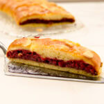 A slice of Easier Danish Pastry sits on a silver cake server with the braid in the background.