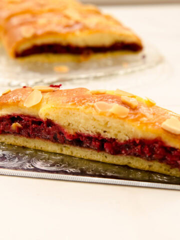 A slice of Easier Danish Pastry sits on a silver cake server with the braid in the background.