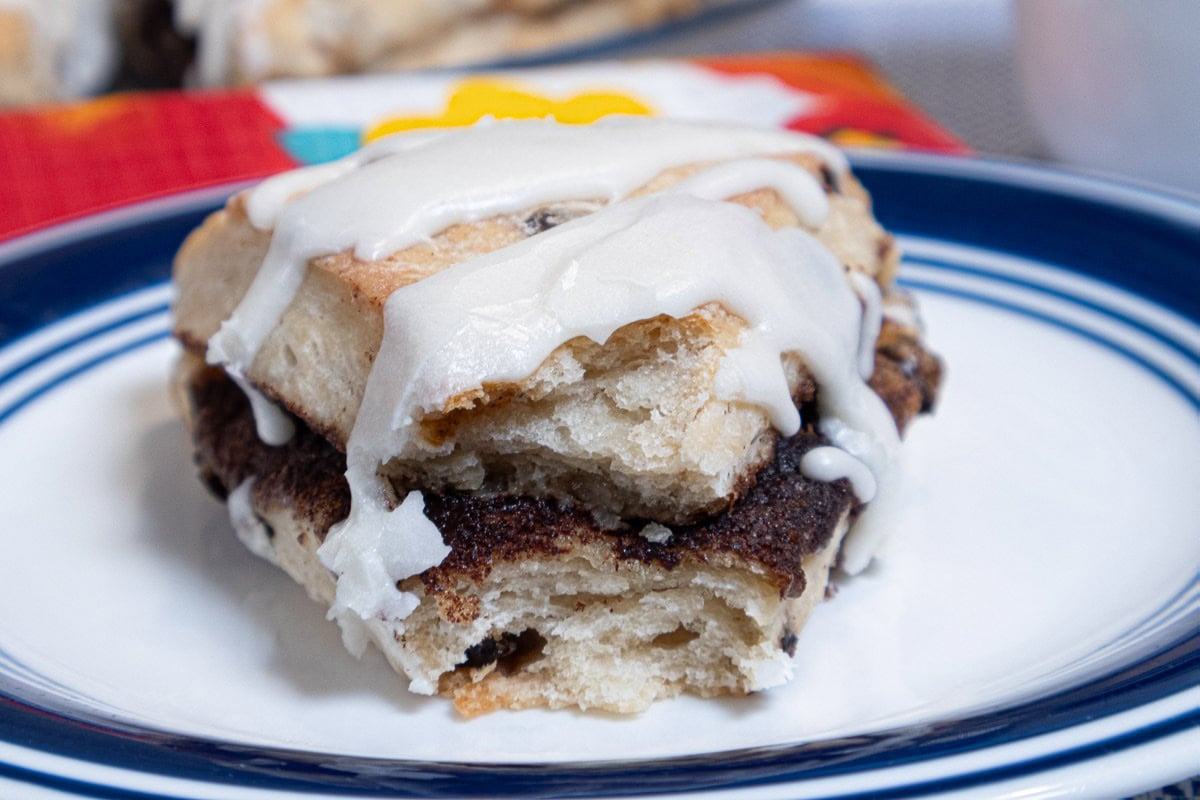 A scone with a bite out of it sits on a blue rimmed plate with a colorful napkin behind it and more scones behind that.