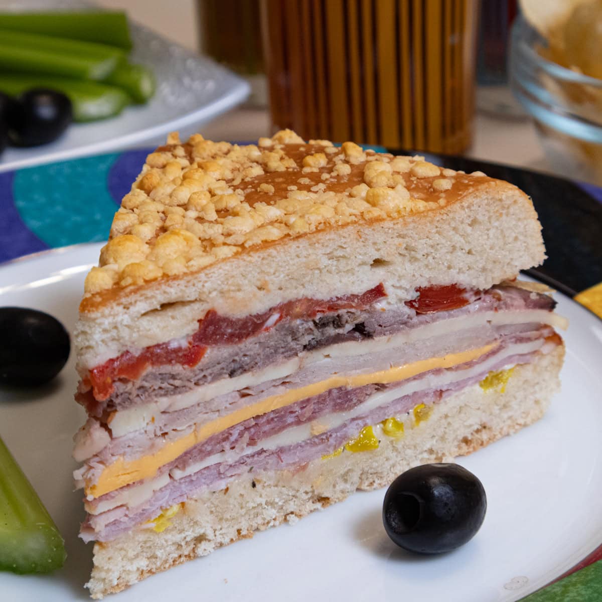 A slice Muffaletta Bread  layered with meats, cheeses and condiments on a plate with olives and celery.