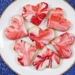 Red and White glazed heart shaped Viennese Lemon Valentines Cookies on a white plate with blue edges.