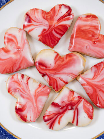 Red and White glazed heart shaped Viennese Lemon Valentines Cookies on a white plate with blue edges.