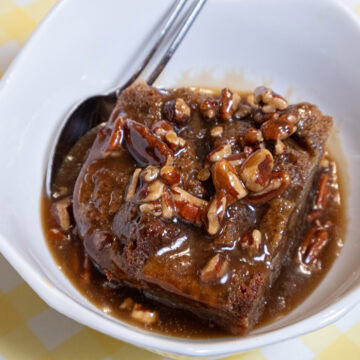 The Banana Bread Bread Pudding sits in a white bowl covered with the bourbon pecan sauce on a yellow and white background.