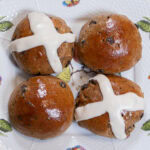 Four Hot Cross Buns sit on an Irish plate with a white background and decorated with little bees and flies.