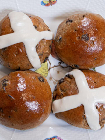 Four Hot Cross Buns sit on an Irish plate with a white background and decorated with little bees and flies.