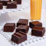 Multiple Mexican Chocolate Browines sit on a white lattice tray with more on a white cake stand with a glass of milk in an orange glass.