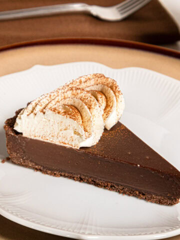A slice of the Cafe au Lait tart sits on a white plate that is on a tan plate with a napkin and fork behind it.
