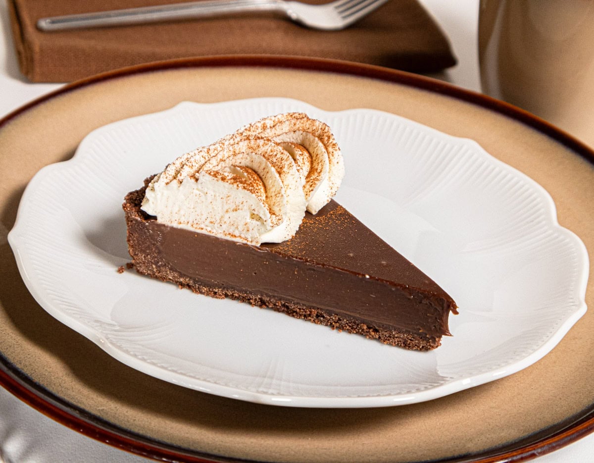 Cafe au lait tart on a white plate that sits on a beige plate with a fork and napkin in the background.