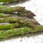 Fresh asparagus spears on a foil lined pan seasoned with salt and pepper.
