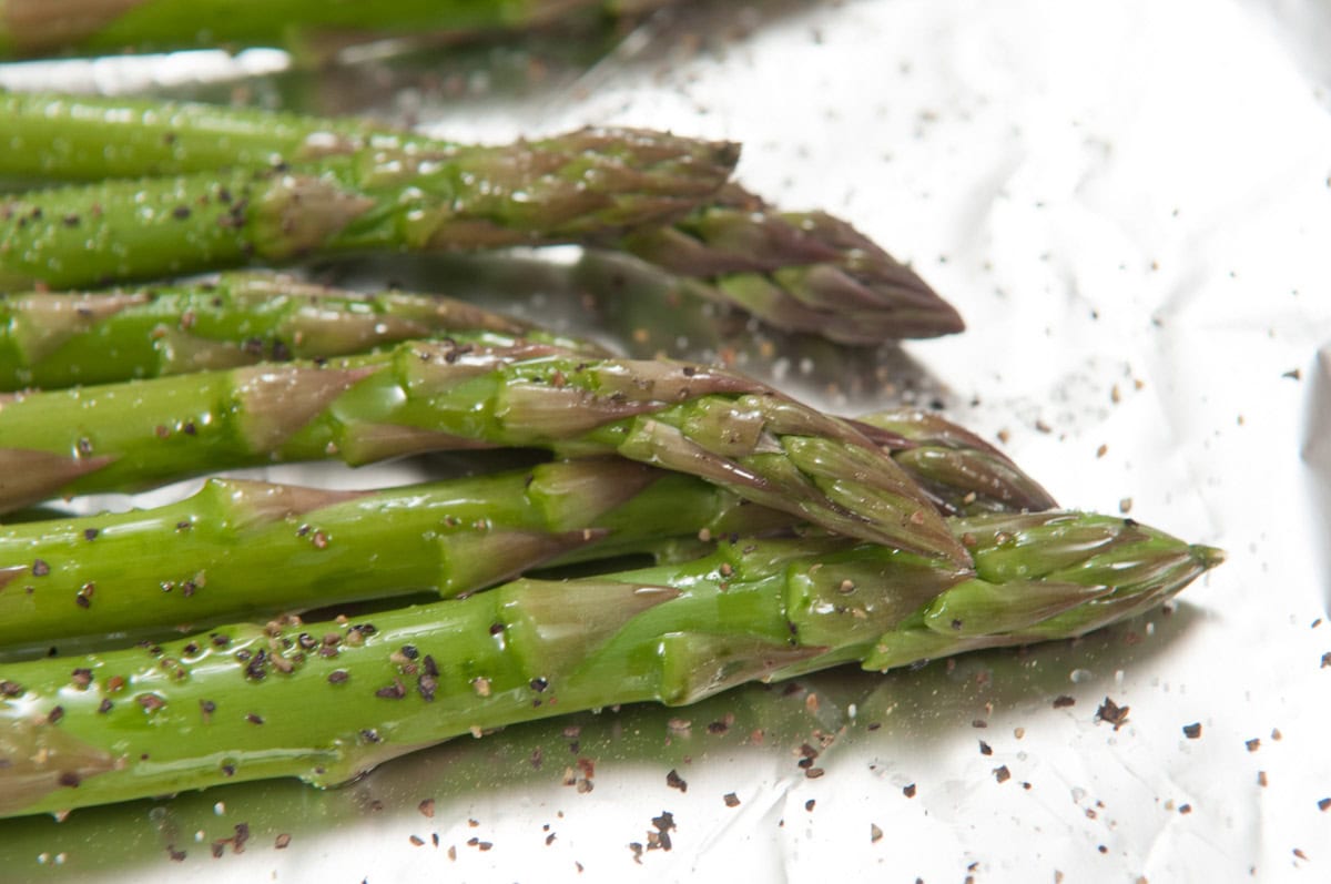 Fresh asparagus spears on a foil lined pan seasoned with salt and pepper.