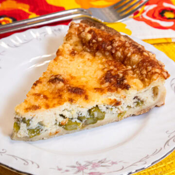 A slice of the Asparagus Tart on a white plate with a colorful napkin and fork in the background.