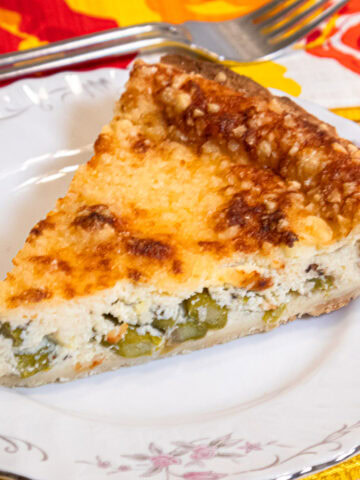 A slice of the Asparagus Tart on a white plate with a colorful napkin and fork in the background.