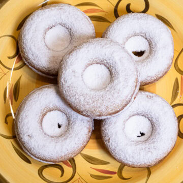 Five Crumbed Baked Donuts sit on a bright yellow and olive green plate covered in powdered sugar.