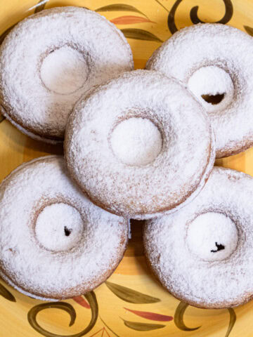 Five Crumbed Baked Donuts sit on a bright yellow and olive green plate covered in powdered sugar.