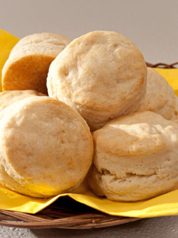 A basket lined wth a yellow napkin is filled with Cream Biscuits.