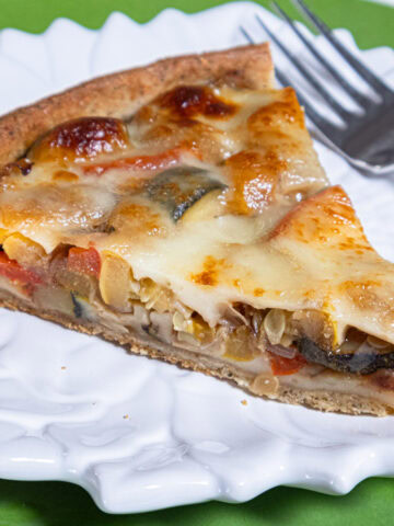 A slice of the Summer Vegetable Tart sits on a white plate with a fork on a green background.