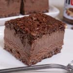 A Nutella Ice Cream Square sits on a w hite plate with more squares behind it and a nutella jar to the side.