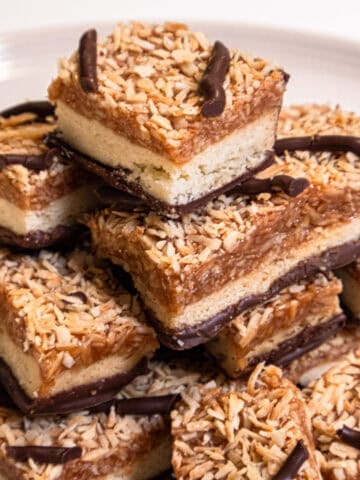 A stack of Samoa Bars sits on a cream colored plate.