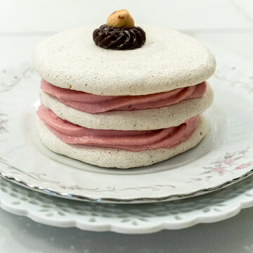 Three meringue discs are filled with raspberry mousse and sit on a pink edged plate.