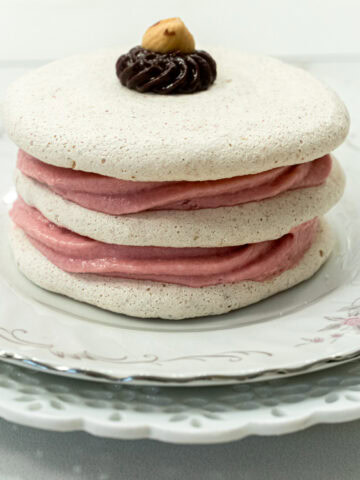 Three meringue discs are filled with raspberry mousse and sit on a pink edged plate.