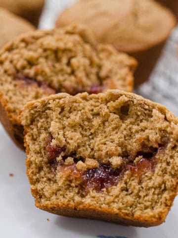 This is a close up of an open Peanut Butter and Jam Muffin with a riverlut of strawberry jam running through it.