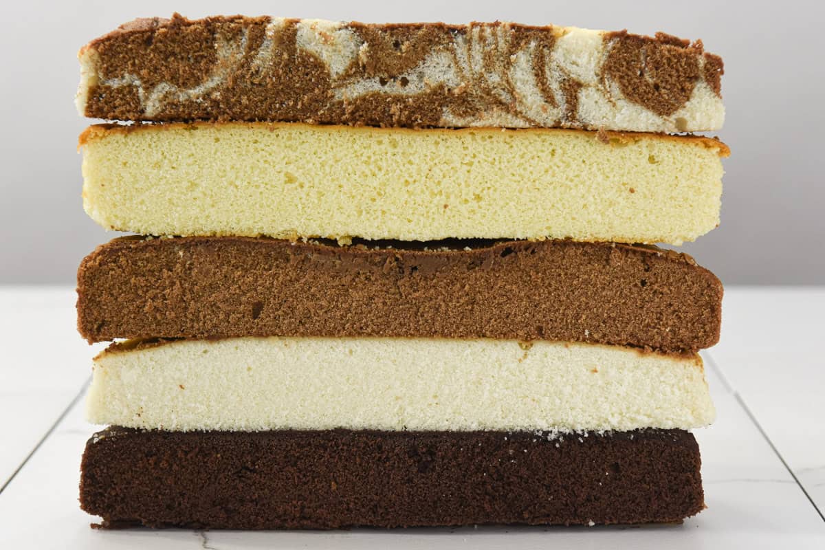 The cut layers of the marble, yellow, white and two chocolate cakes are stacked on top of each other. 