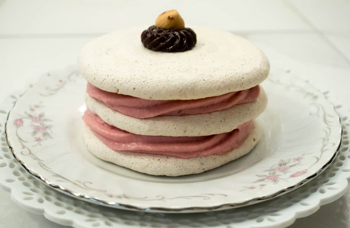 Three meringue discs are filled with raspberry mousse and sit on a pink edged plate.