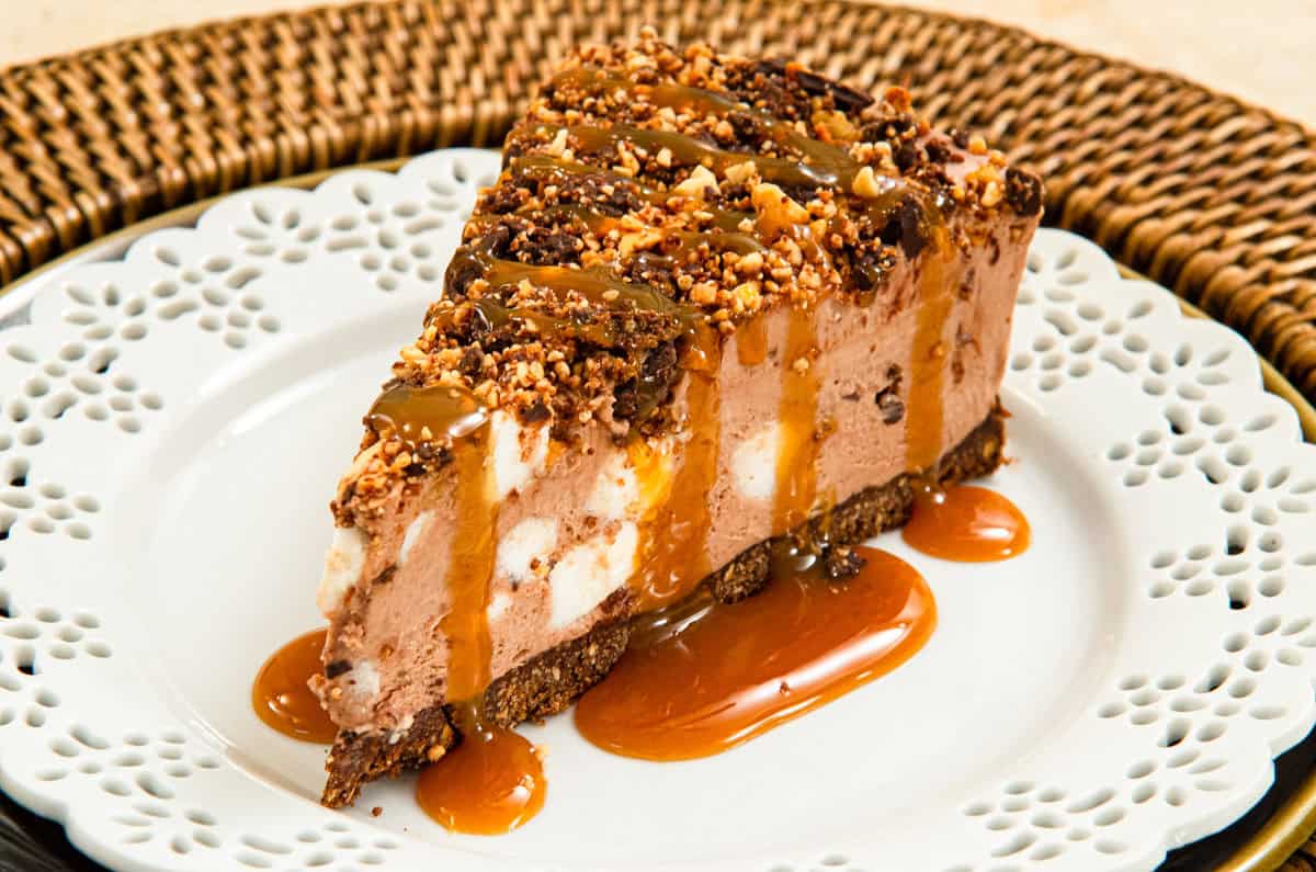 A slice of the Rocky Road Cheesecake sits on a white plate on a rattan server.