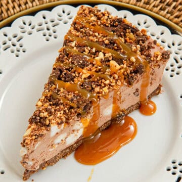 A slice of the Rocky Road Cheesecake sits on a white plate on a rattan server.