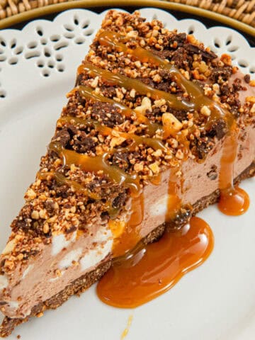 A slice of the Rocky Road Cheesecake sits on a white plate on a rattan server.