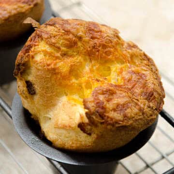 A single Cheddar Bacon Popover in it's pan sits on a cooling rack.