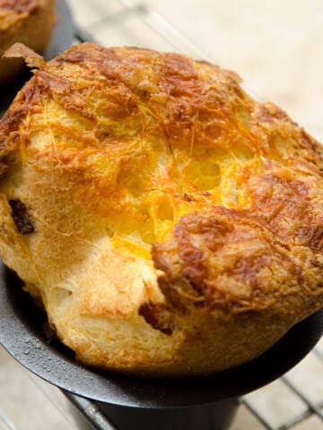 A single Cheddar Bacon Popover in it's pan sits on a cooling rack.