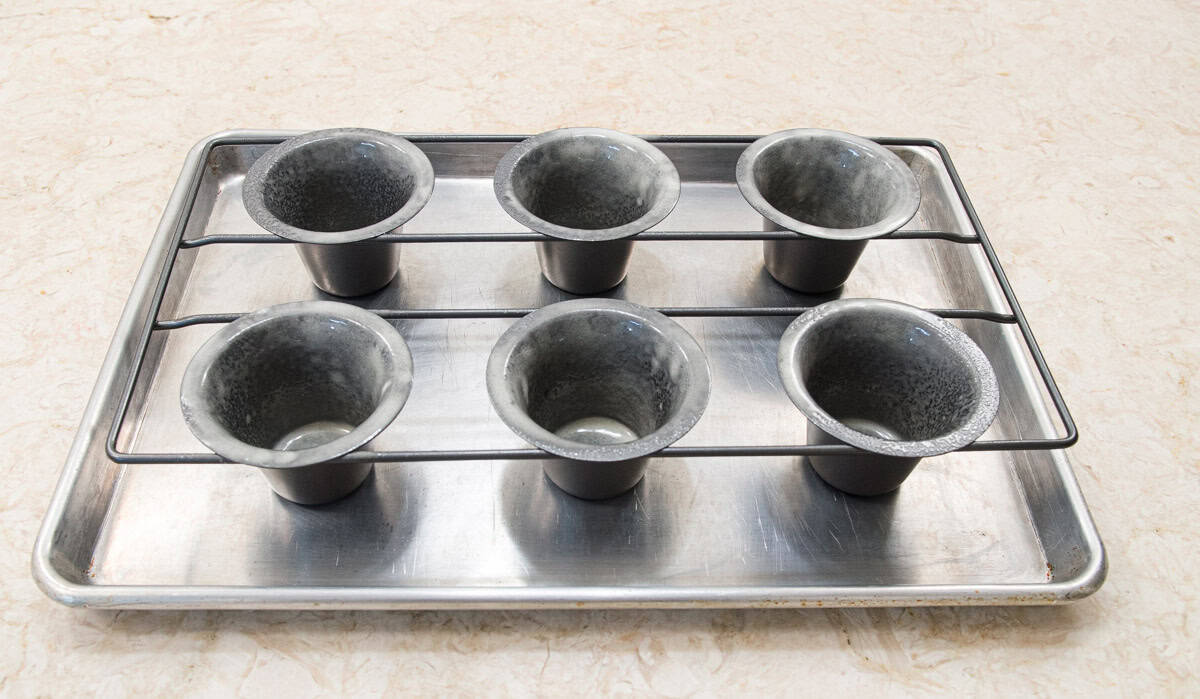 A rack of 6 popover molds sits on a baking pan. 