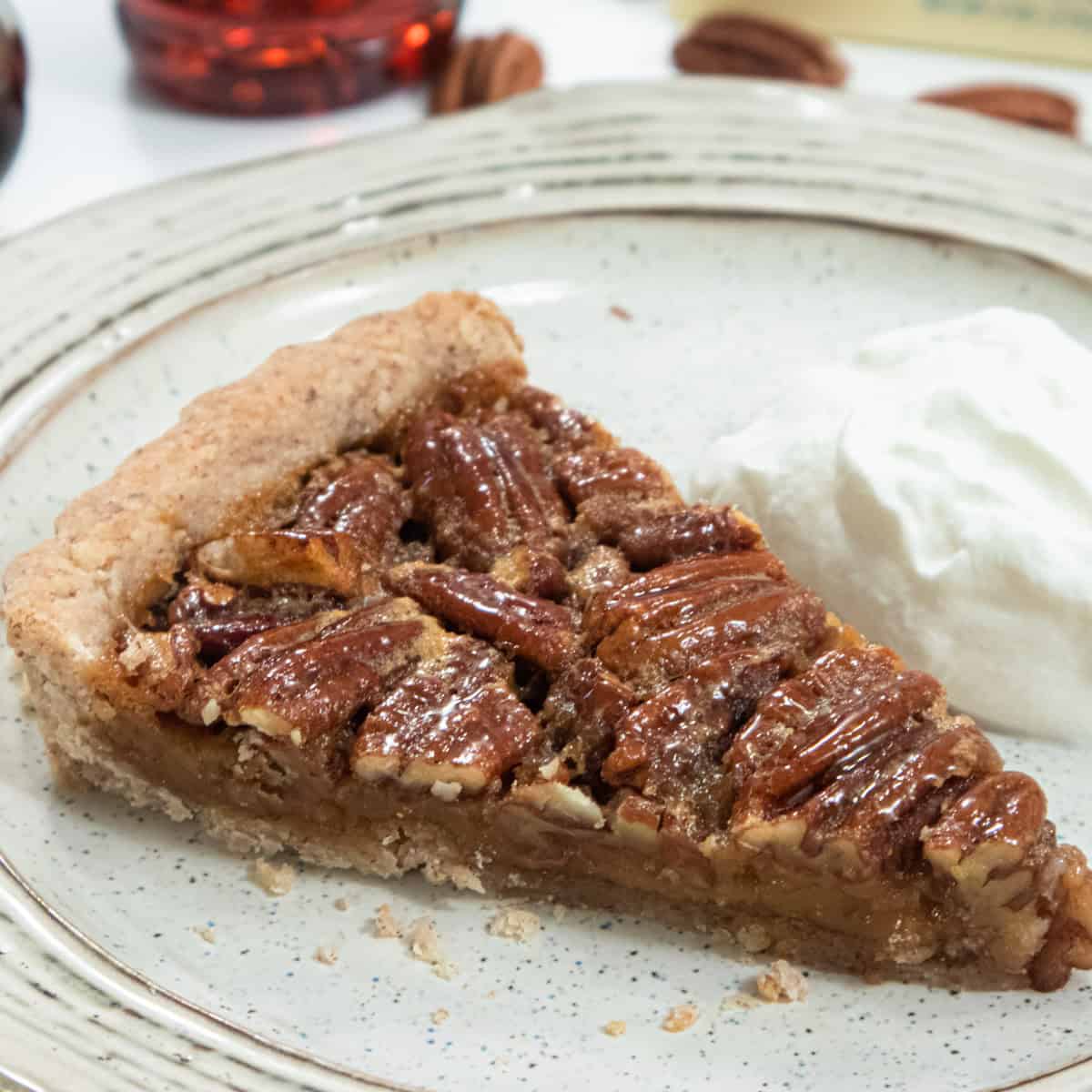 A slice of the Butter Run Pecan Tart sists on a brown striped plate with a dollup of whipped cream.