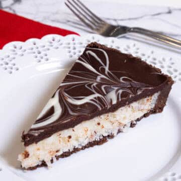A slice of the Chocolate Coconut Tart sits on a lace edged white plate with a red napkin and a fork behind it.
