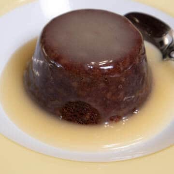 An individual Sticky Toffee Pudding sits in a puddle of Lemon Sauce in a yellow and white bowl.