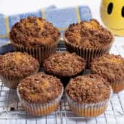 Really Easy Pumpkin Muffins on a cooling rack with a yellow happy face mug in the background and a blue and yellow towel.