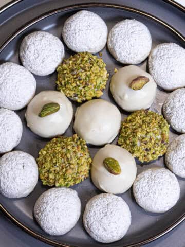 A tray of White Chocolate Pistachio Cookies finished 4 different wasys its on a gray plate rimmed in gold.