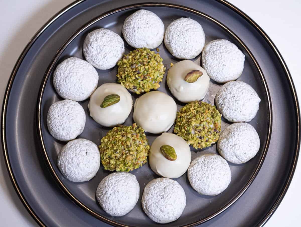 A tray of White Chocolate Pistachio Cookies finished 4 different wasys its on a gray plate rimmed in gold. 