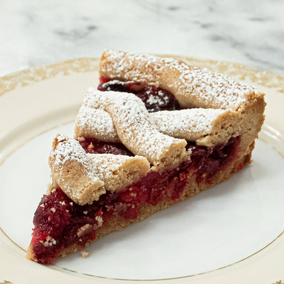 A slice of the Cranberry Linzer Tart sits on an antique cream and gold plate.